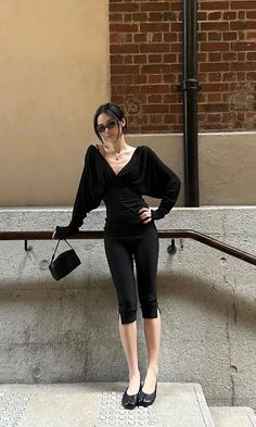 Woman in a black outfit and sunglasses posing on stairs indoors