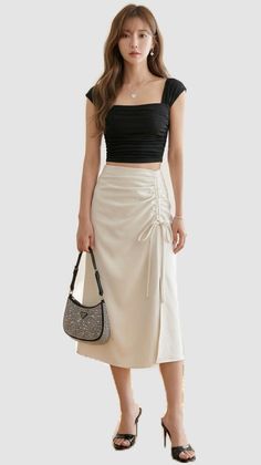 Woman in a black crop top and white midi skirt holding a studded shoulder bag