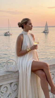 Woman in a white dress holding a wine glass at sunset by the water