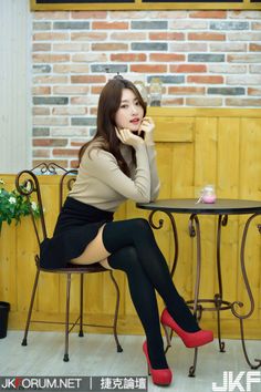 Woman in a beige turtleneck, black mini skirt, and thigh high socks sitting indoors