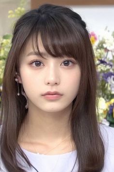 Woman with long brown hair and bangs wearing earrings and a necklace