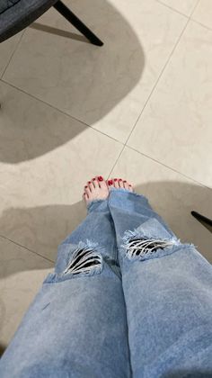 Person wearing ripped jeans with bare feet and red nail polish on a tiled floor