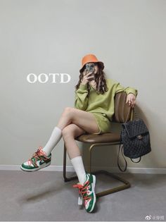 Person in a green outfit and orange bucket hat sitting on a chair indoors