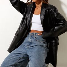 Woman in a black leather jacket, white crop top, and blue jeans