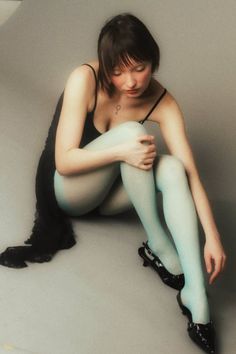 Woman in a black dress and blue tights sitting on a gray floor