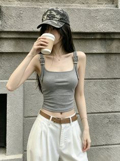 Woman in a camo hat and gray tank top drinking from a cup outdoors
