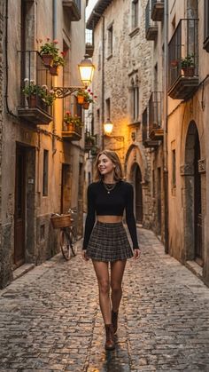 Woman in a plaid skirt and crop top walking down a cobblestone street at dusk