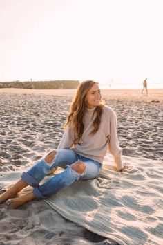 Woman with long hair sitting on a blanket on the beach at golden hour