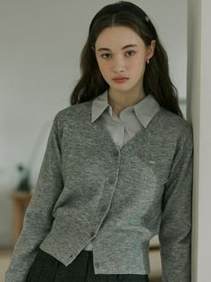 Woman with long hair wearing a gray cardigan and collared shirt indoors