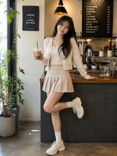 Woman in a pleated skirt and crop top holding an iced coffee in a cafe