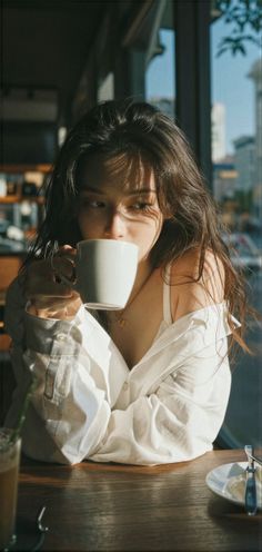 Woman in a white shirt drinking from a mug with dappled sunlight on her face
