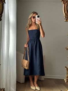 Woman in a navy midi dress and sunglasses taking a mirror selfie