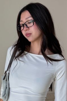 Woman with long dark hair and glasses wearing a white top and carrying a shoulder bag