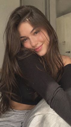 Woman with long brown hair wearing an off-shoulder top and grey sweatpants