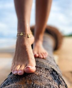 Bare feet with an anklet balancing on a wet tree trunk