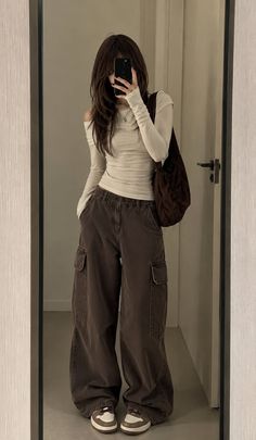 Person with long hair taking a mirror selfie in an off-shoulder top and cargo pants