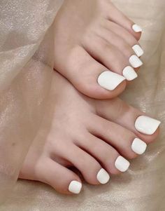 Close up of feet with white painted toenails on a soft fabric surface