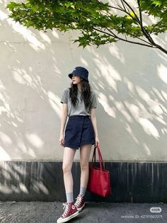 Woman in a bucket hat and mini skirt holding a red tote bag outdoors