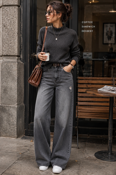 Woman in a dark gray sweater and wide leg jeans holding a coffee cup outdoors