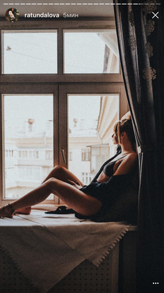 Woman in a bra and open shirt sitting on a windowsill looking out