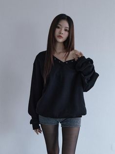 Woman in a black sweatshirt, denim shorts, and black tights posing indoors