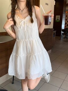 Person in a white tiered dress with braided hair holding a drink indoors