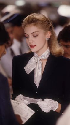 Blonde woman in a suit jacket, silk scarf, and white gloves looking down