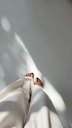 Bare feet with dark nail polish and white pants on a sunlit floor