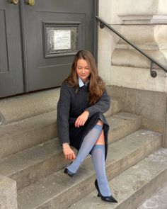 Woman with long hair sitting on stone steps wearing a gray sweater and blue socks