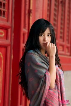 Woman with long dark hair wearing a patterned shawl against a red background