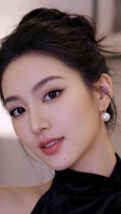 Woman with black hair in an updo wearing pearl earrings and glossy lips