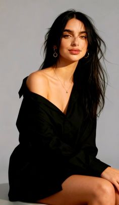 Woman with long dark hair wearing a black shirt with an exposed shoulder