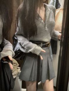 Person in a grey sweater and pleated skirt reflected in a mirror
