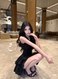 Woman in a black dress and high heels squatting in a hotel lobby
