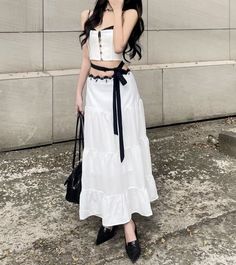 Woman in a white crop top and maxi skirt with a black ribbon and handbag