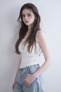 Woman with long brown hair wearing a white tank top and light wash jeans