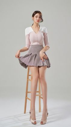 Woman in a pink top and pleated skirt posing on a stool