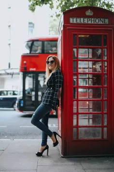Woman in a plaid blazer and jeans leaning against a red telephone booth
