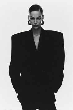 Woman in a black blazer with slicked back hair and large earrings