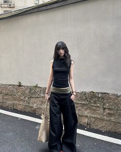 Woman with long black hair wearing a black top and wide leg pants on a street