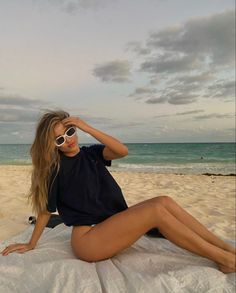 Woman with long hair and sunglasses sitting on a beach with an ocean background