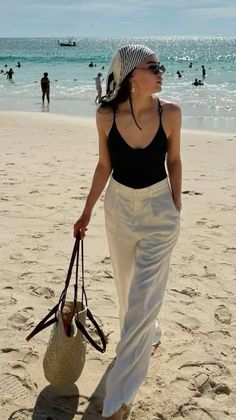 Woman in a black top and white pants walking on a sandy beach