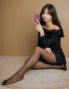 Woman in a black dress and tights sitting on a rug taking a selfie