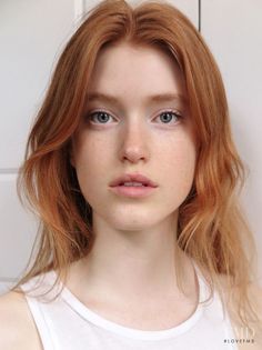 Woman with red hair and blue eyes wearing a white tank top