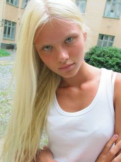 Young woman with long blonde hair and blue eyes wearing a white tank top outdoors