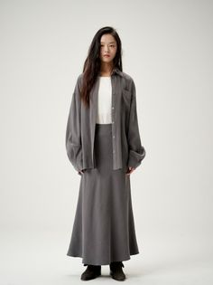 Woman with long dark hair wearing an oversized shirt and long skirt in a studio