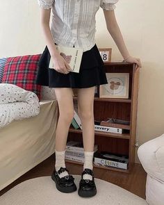 Person in a white blouse and black skirt holding a book indoors