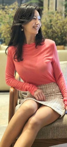 Woman in a coral shirt and mini skirt sitting indoors