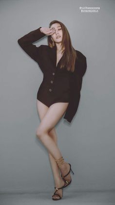 Woman in a black blazer and high heels posing against a gray wall