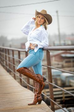 Woman in a cowboy hat, white shirt, jeans, and cowboy boots on a bridge